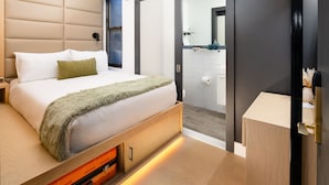 Un dormitorio moderno con cama, almacenaje integrado, una puerta corredera hacia el baño y una mesita de noche de madera.