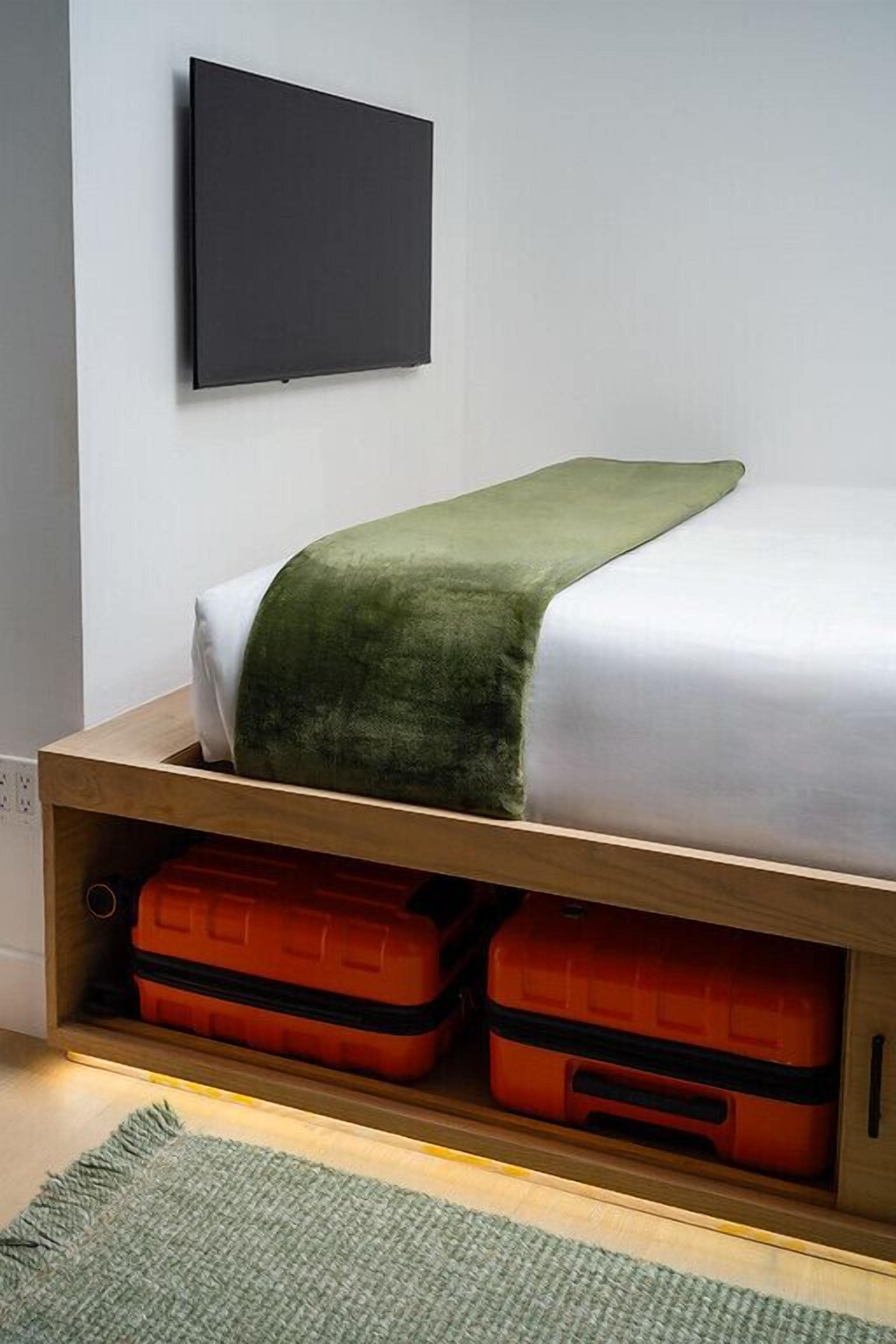 A bed with a green blanket, a white mattress, and two orange suitcases under the bed.
