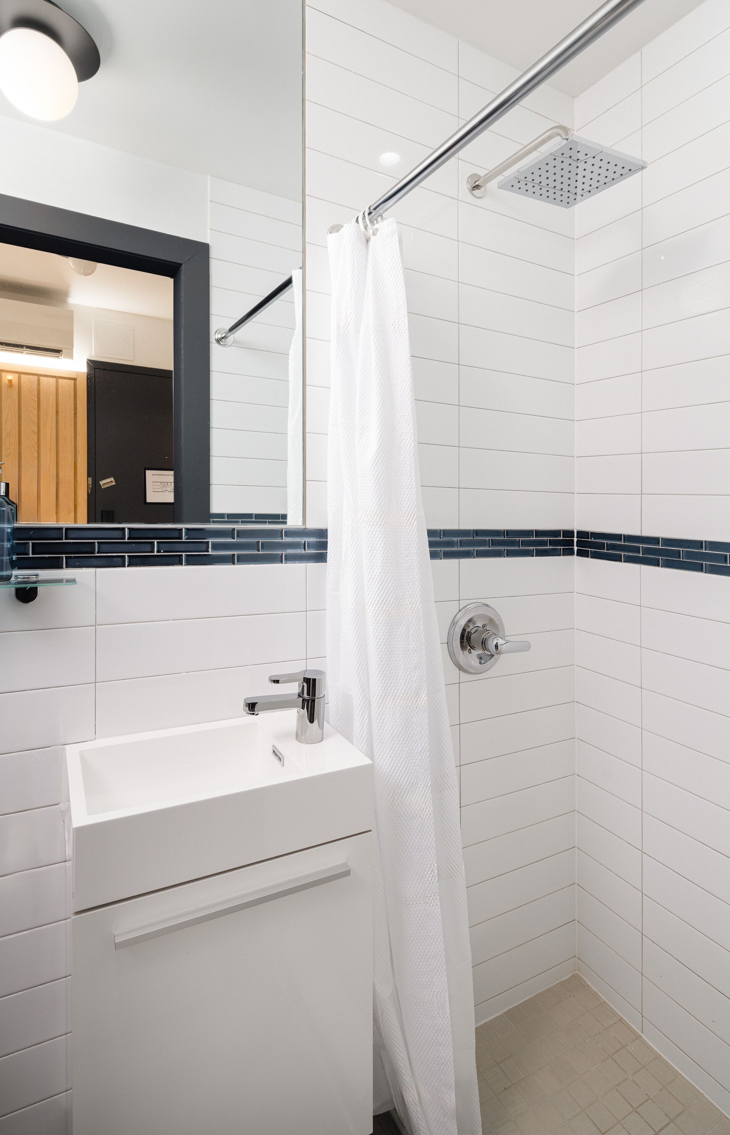 Une salle de bain moderne avec des carreaux blancs, un lavabo blanc et une douche dotée d’une porte en verre.