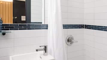 Une salle de bain moderne avec des carreaux blancs, un lavabo blanc et une douche dotée d’une porte en verre.