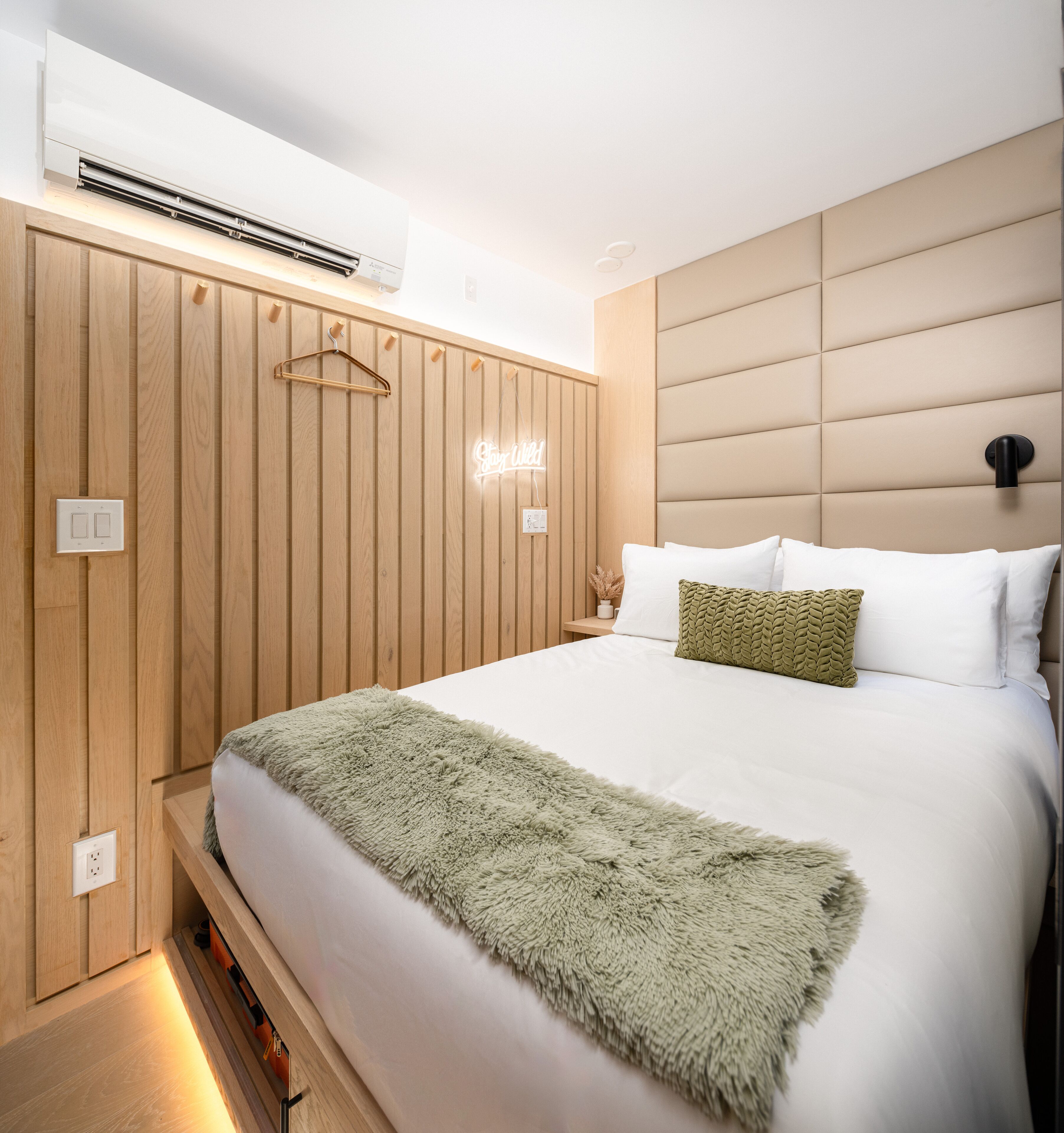 Un dormitorio moderno con una cama grande, paneles de madera, un colgante de luz y un letrero de neón.
