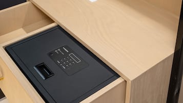 A compact workspace with a wooden desk, a black electronic device, a white vase with dried flowers, and a remote control.
