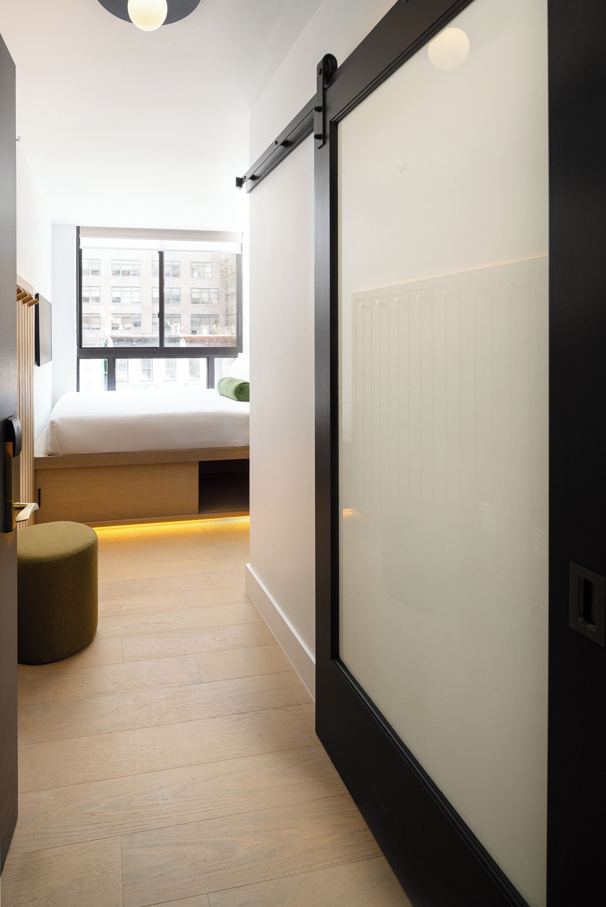 A narrow hallway leading to a bedroom with a bed, a window, and a sliding door.