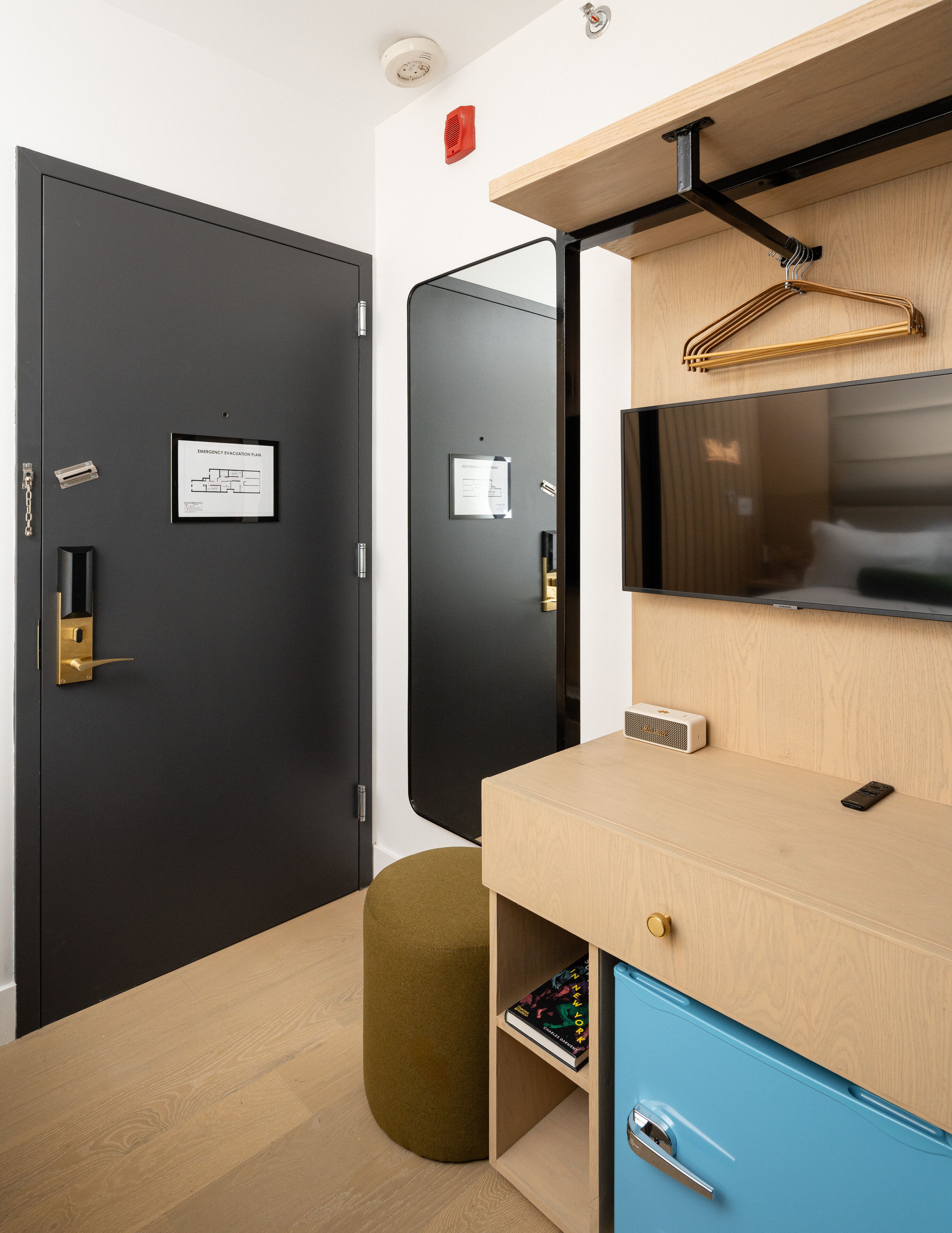 A modern room with a black door, a wooden desk, a blue cabinet, and a mounted TV.