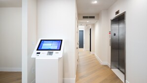 Un pasillo con un quiosco digital, un ascensor y una puerta que da a otra habitación.
