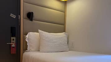 Uma cama de solteiro com cabeceira, uma luminária de cabeceira e uma gavetinha sob a cama.