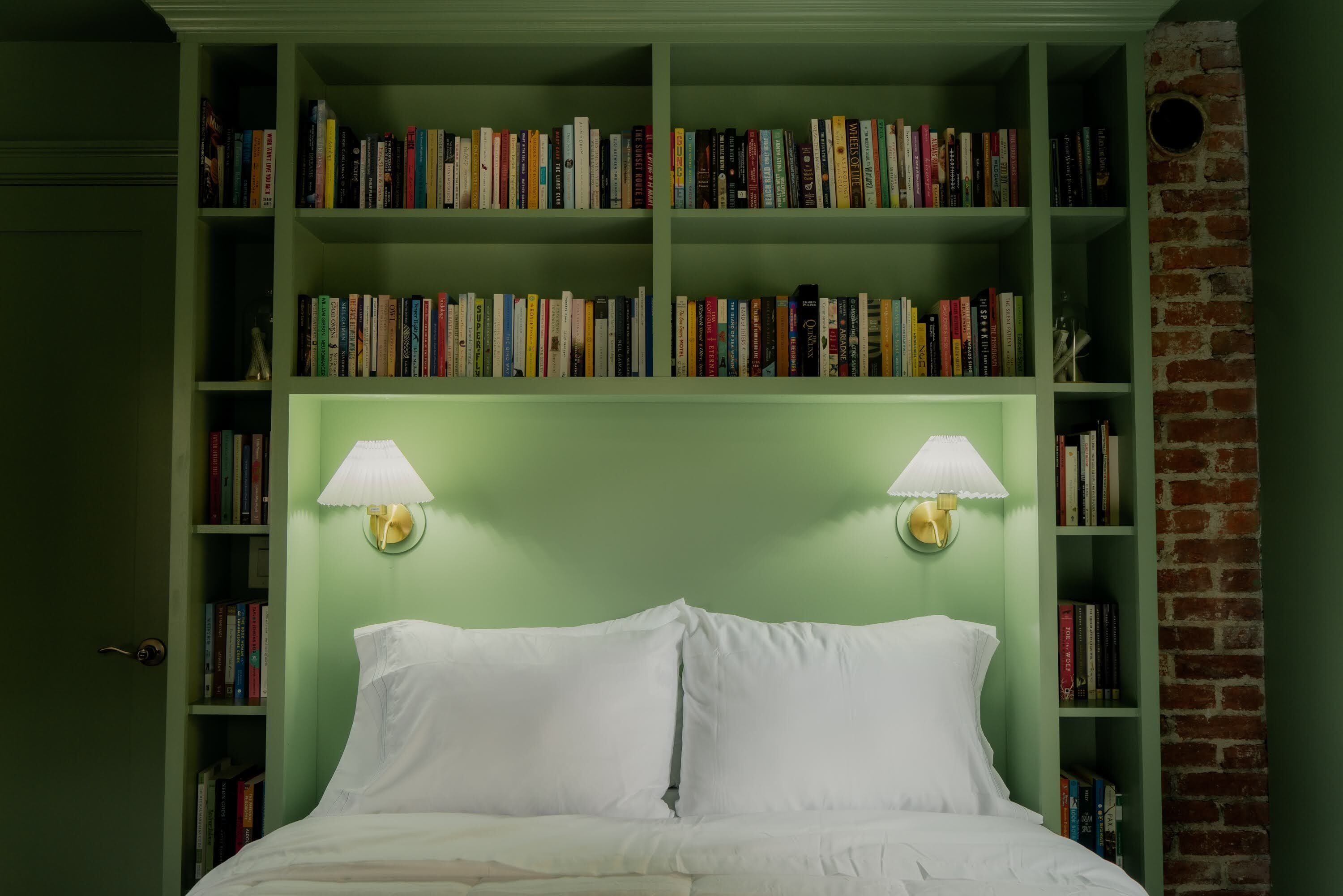 Une chambre avec un mur vert, un lit blanc et des étagères remplies de livres.
