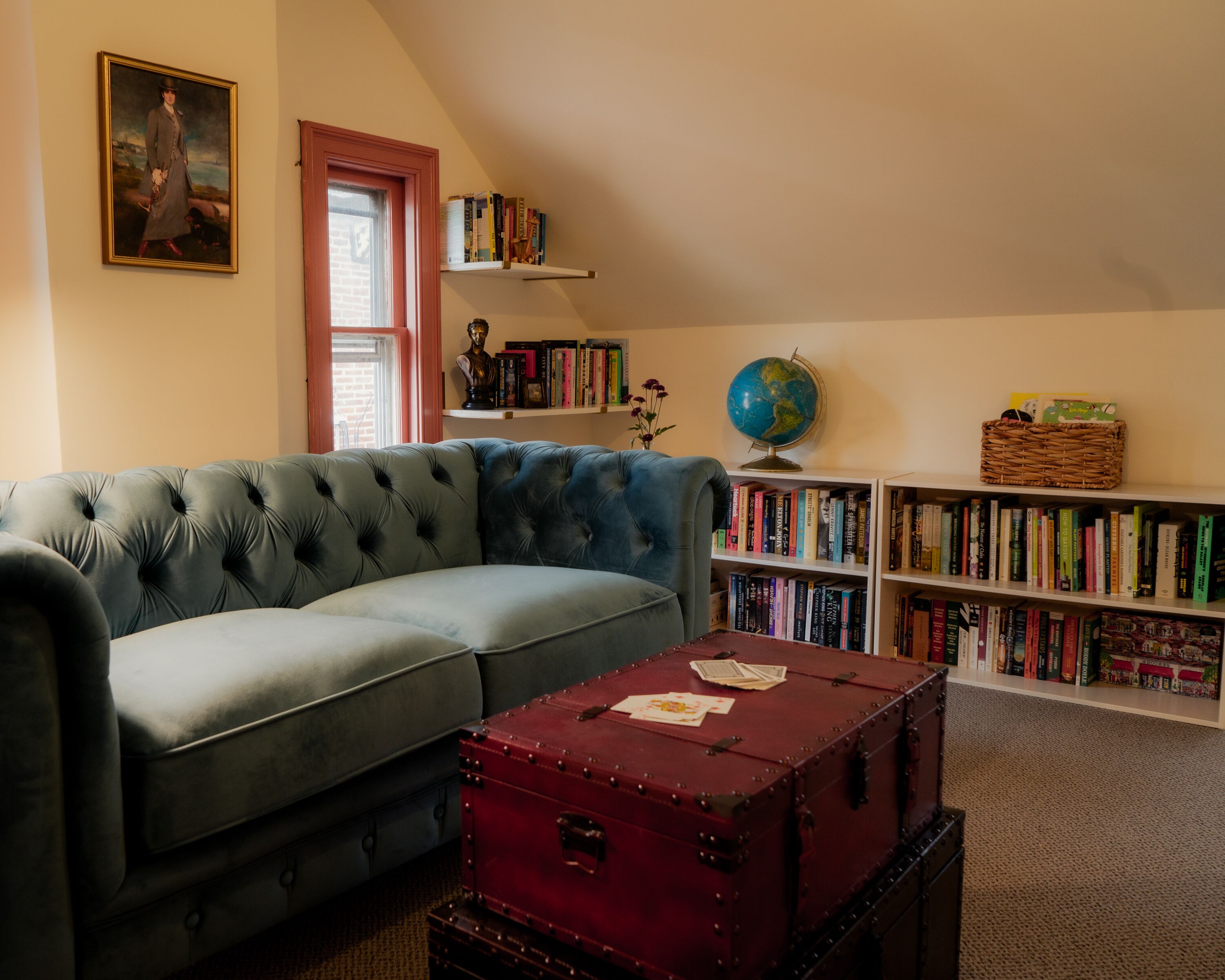 Una habitación con un sofá azul, un baúl rojo, estanterías y un globo terráqueo.