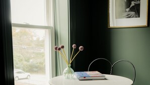 Une pièce avec une table ronde, une chaise, un vase de fleurs et un tableau encadré au mur.