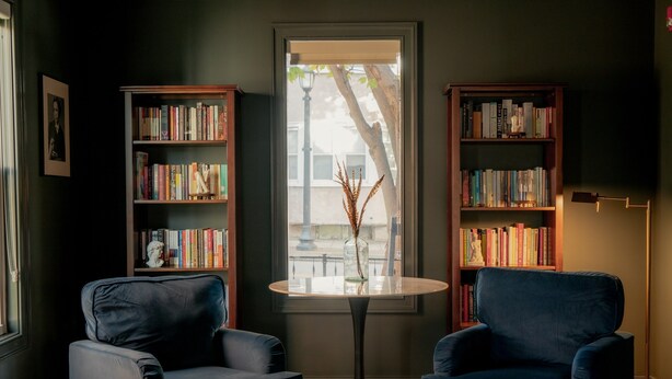 Une pièce avec deux fauteuils bleus, une table ronde et deux étagères en bois remplies de livres.