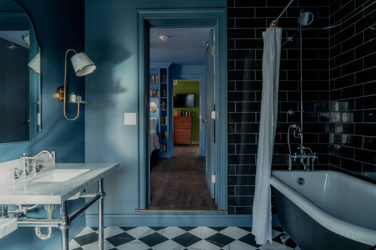 A bathroom with a white bathtub, a sink, and a mirror. There is a door leading to a hallway with a wooden floor and a green wall.