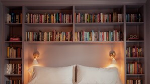 Une chambre à coucher bien rangée, avec un grand lit, deux lampes de chevet et une bibliothèque remplie de livres.