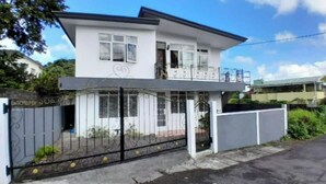 Una casa de dos pisos con entrada protegida por un portón, y un balcón en el nivel superior, bajo un cielo despejado.