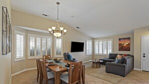 A spacious living area with a dining table, chairs, a gray sofa, and a chandelier. - Large 5 Bedroom Home - Family Getaway w/ Pool (Turlock)