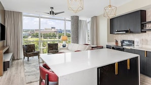 Une cuisine moderne dotée d’un îlot central, de meubles de rangement aux couleurs sombres et d’une grande fenêtre offrant une vue sur la ville.
