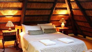 A cozy attic bedroom with a sloped ceiling, a large bed with white linens, two bedside lamps, and a wooden nightstand.