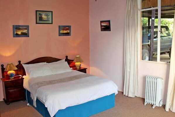 A bedroom with a bed, two bedside tables with lamps, a radiator, and a window with curtains.