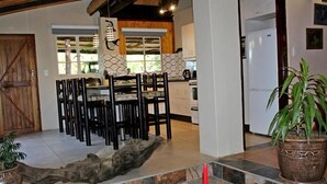 A spacious kitchen with a dining area, featuring a rustic wooden door, a large dining table with chairs, and a potted plant.