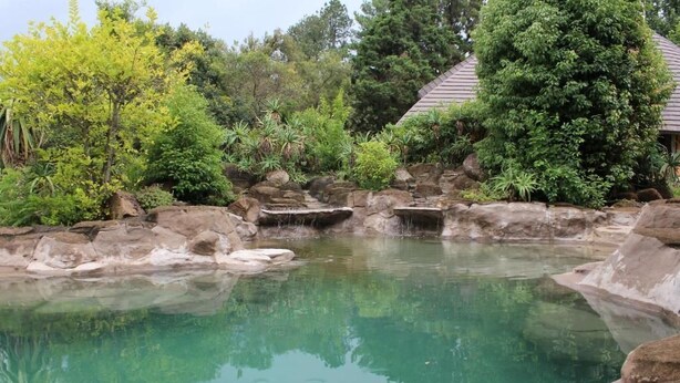 A tranquil outdoor pool area with clear water, surrounded by rocks and lush greenery.