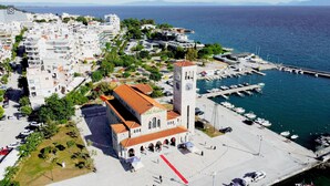 Vue aérienne d’une ville côtière, avec une église imposante dotée d’un clocher, un port de plaisance avec des bateaux et des immeubles d’habitation.