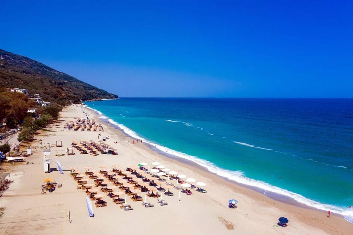 A beach with rows of sun loungers and umbrellas, a clear blue sky, and the ocean.