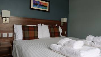 A hotel room with a large bed, white linens, plaid pillows, and a framed picture on the wall.