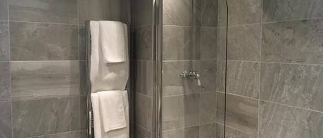Casa de banho moderna com chuveiro em cabine de vidro, banheira e toalheiro com duas toalhas brancas.