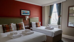 A hotel room with two beds, each with white linens and folded towels. There is a painting on the red wall above the beds, a window with curtains, and a mirror on the wall. - The Portree Hotel  (Portree)