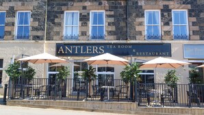 A hotel with a stone facade, outdoor seating area with umbrellas, and a sign for the Antlers Tea Room & Restaurant. - The Portree Hotel  (Portree)