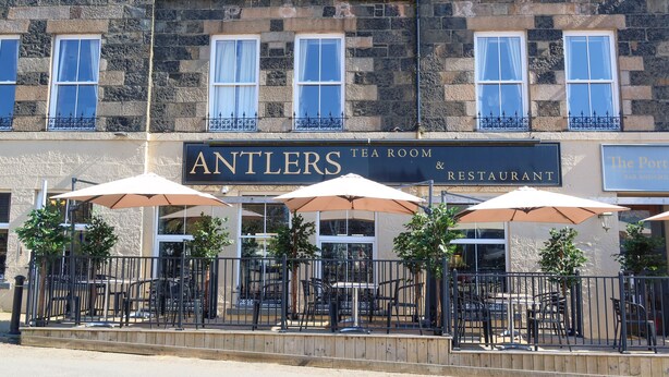 Ein Hotel mit Steinfassade, Außenbereich mit Sonnenschirmen und einem Schild für das Antlers Tea Room & Restaurant.
