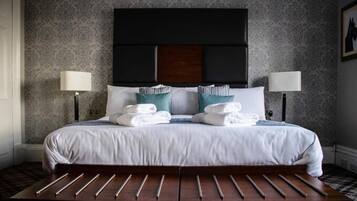 A neatly made bed with white linens and teal pillows, flanked by two bedside lamps.