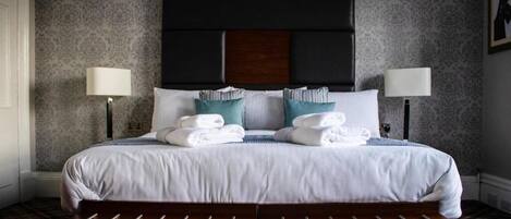 A neatly made bed with white linens and teal pillows, flanked by two bedside lamps.