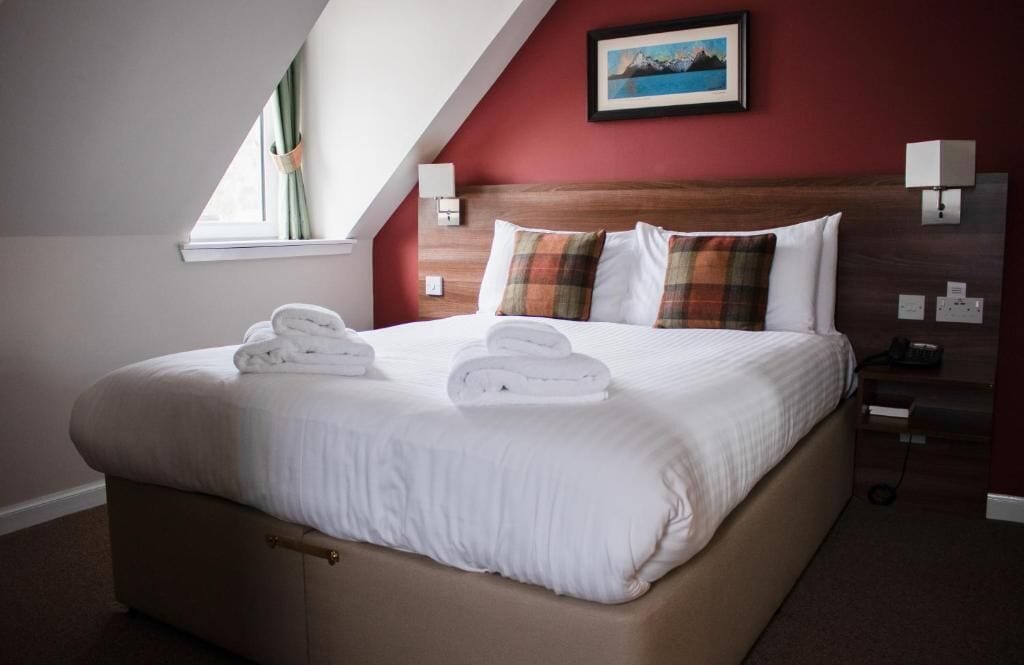 A neatly made bed with towels, a wooden headboard, and a painting above it.