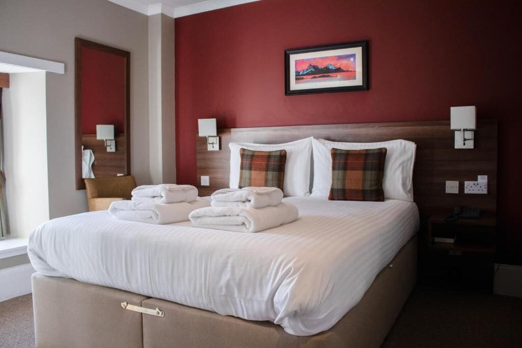 A neatly made bed with white linens and folded towels, a wooden headboard, and a framed picture on the wall.