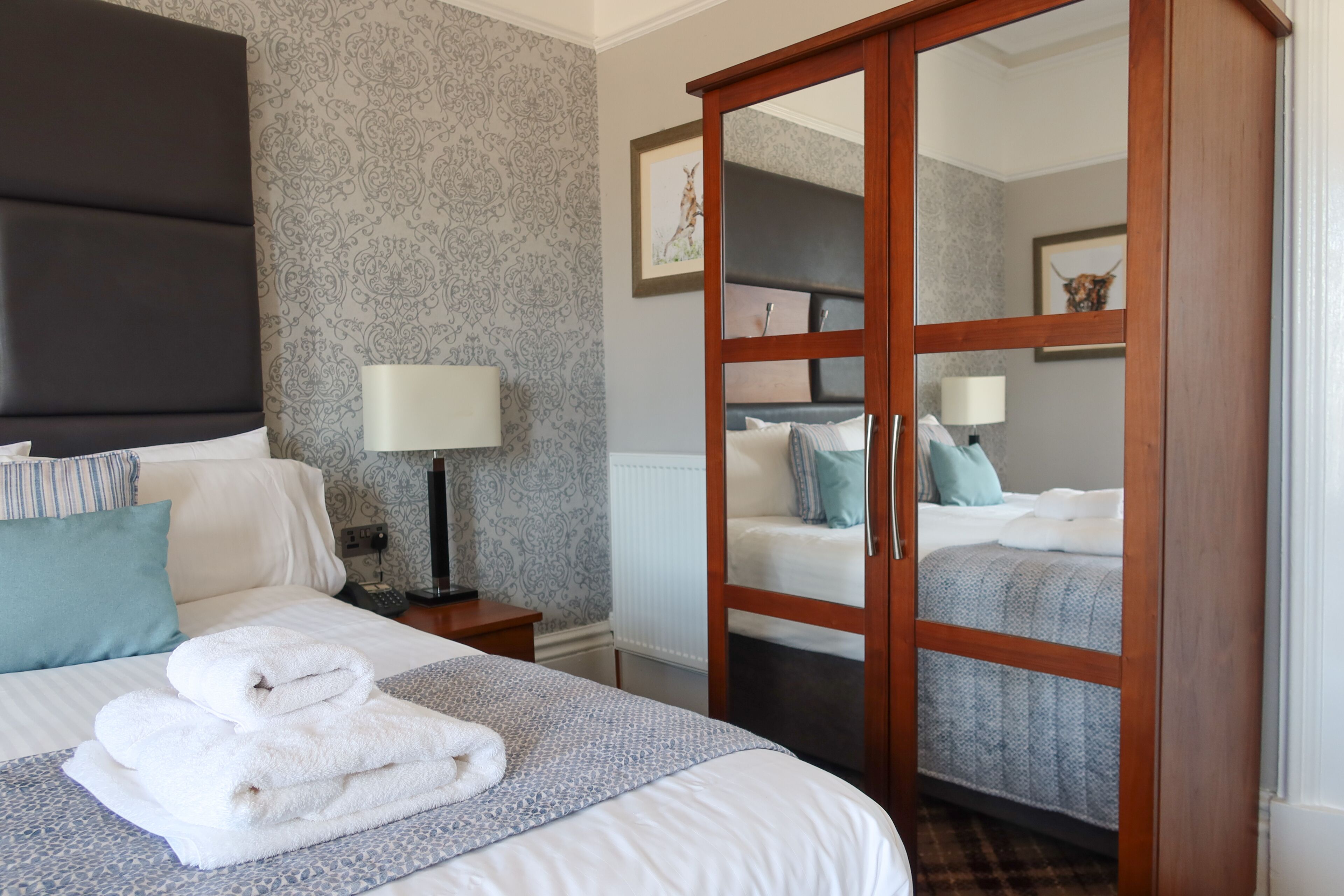 A hotel room with a bed, a nightstand, a lamp, a wardrobe, and a mirror.