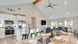 A spacious kitchen with modern appliances, a dining area with a long table set for four, and a cozy living area with a sofa and TV.