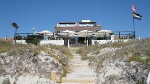 A coastal building with multiple levels, outdoor seating with umbrellas, and a flag on a flagpole. - Hotel Maluentu (San Vero Milis)