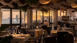 A restaurant with tables set for dining, a bar area, and a view of the sea. - Hotel Maluentu (San Vero Milis)