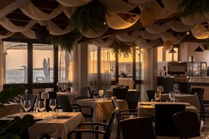 Un restaurante con mesas dispuestas para comer, una zona de bar y vistas al mar.