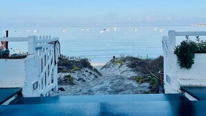 A coastal view with a white fence leading to a sandy beach, a clear sky, and boats in the distance. - Hotel Maluentu (San Vero Milis)