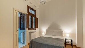 Une chambre à coucher comprenant un lit, deux lampes de chevet, un radiateur et une porte donnant sur une salle de bain.