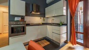 Une cuisine moderne dotée d’appareils électroménagers en acier inoxydable, de meubles blancs et d’une fenêtre agrémentée de rideaux orange.