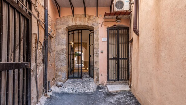 Une ruelle étroite aux murs de pierre et aux portails en métal.