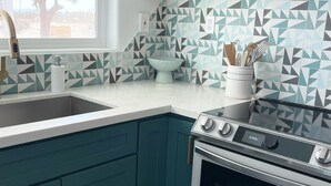 A kitchen with teal cabinets, a white countertop, a built-in oven, and a window with a view of a tree. - Serenity Now / Spa+Outdoor Shower+Hammocks+RV h/up (Landers)