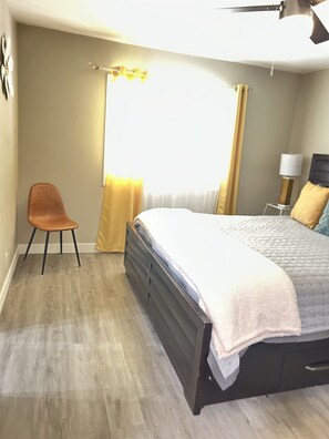 A bedroom with a bed, a chair, a nightstand, and a window with curtains.