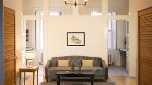 Un salon spacieux avec un canapé gris, un lustre et un tableau encadré au mur.