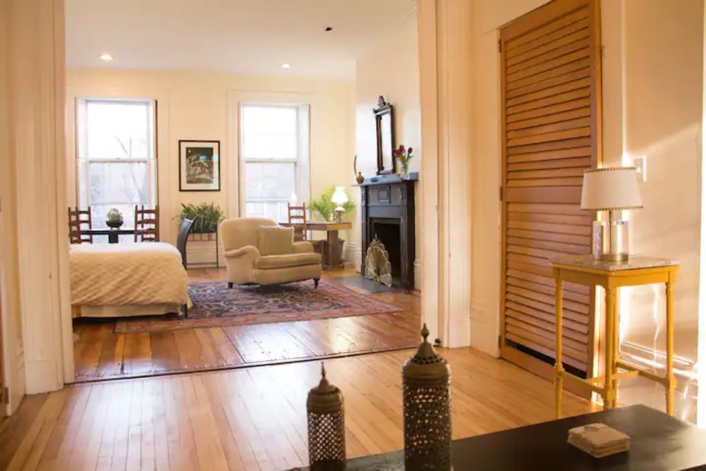 A spacious room with a large bed, a chair, a fireplace, and a table with a lamp.