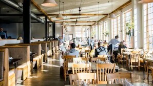 Un restaurant spacieux avec des tables et des bancs en bois, de grandes fenêtres et des lampes suspendues.