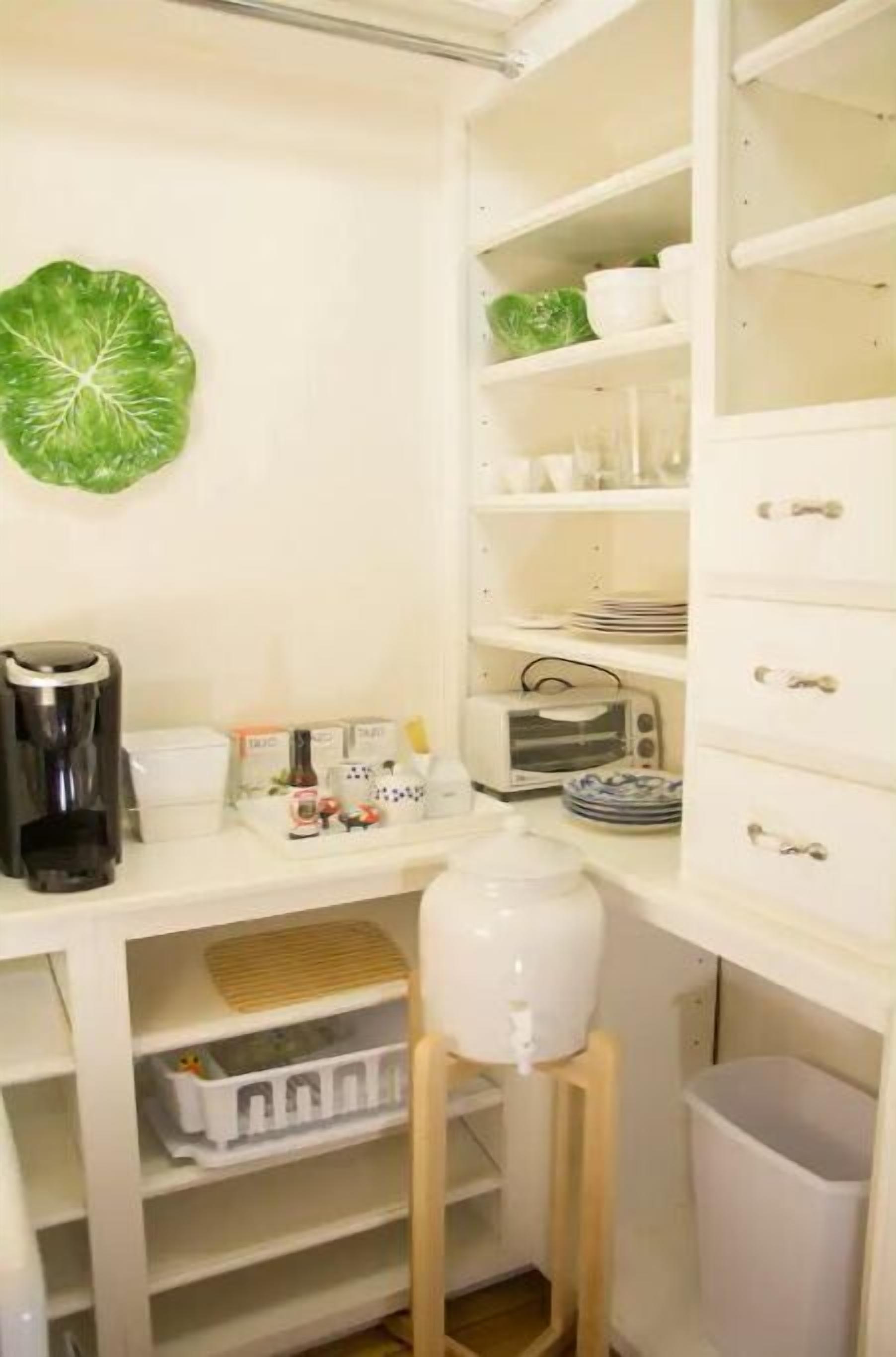 Una cocina con armarios blancos, una cafetera, un tostador y un cubo de basura.