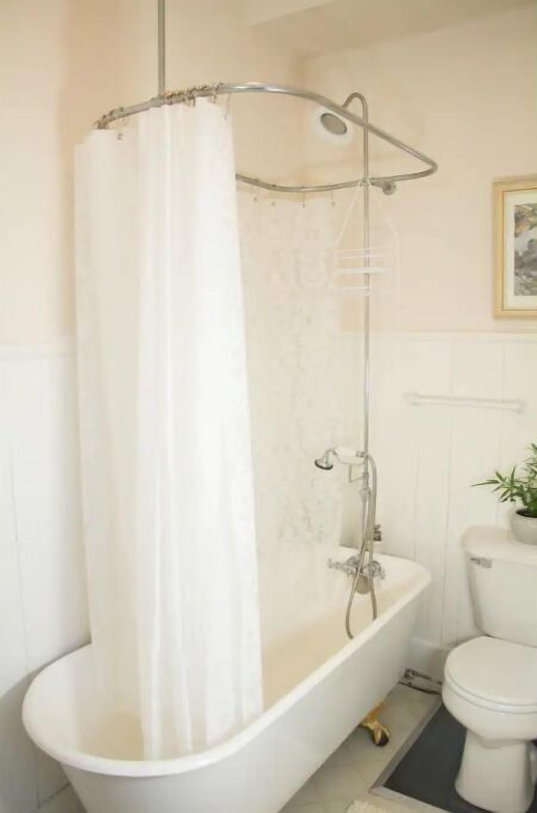A bathroom with a white bathtub, a shower curtain, a toilet, and a framed picture on the wall.